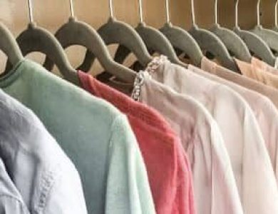 In einem Schrank hängende Kleidung, darunter Hemden und Blusen in verschiedenen Farbtönen auf Kleiderbügeln.
