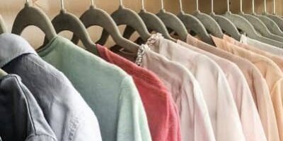 In einem Schrank hängende Kleidung, darunter Hemden und Blusen in verschiedenen Farbtönen auf Kleiderbügeln.