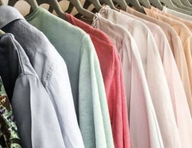 In einem Schrank hängende Kleidung, darunter Hemden und Blusen in verschiedenen Farbtönen auf Kleiderbügeln.